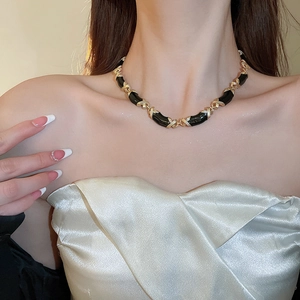 Détail des maillons en X noir et or sur un collier en émail au style vintage chic
