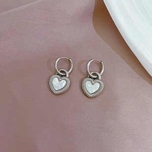 Macro detail of shell heart earrings with silver metal finish and radiating texture on pink fabric