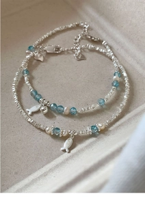 Detailed macro of silver fish charm and sea blue crystal beads on a pearl bracelet