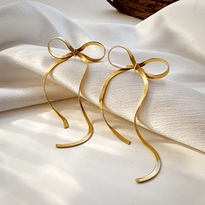 Detailed view of golden bow earrings with elegant fringe tassels on white fabric