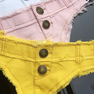 Dettaglio macro di pantaloncini in denim rosa e gialli con bordi sfilacciati e doppi bottoni