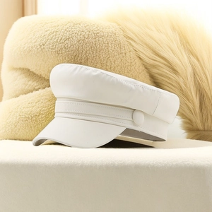 White PU leather baker boy cap with flat top design on a soft beige plush background