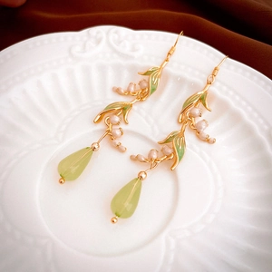 Détail macro des boucles d'oreilles muguet avec feuilles vertes et perles goutte