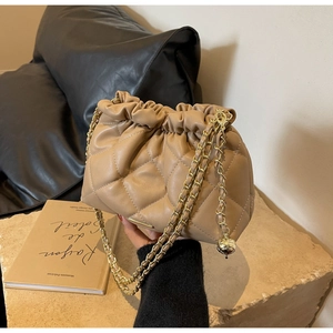 Detail of khaki quilted chain bucket bag with gold ball accent on stone surface
