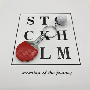 Close-up of a mini red table tennis paddle and ball keychain on a white decorative card