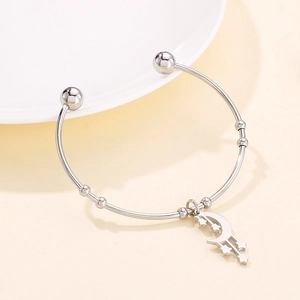 Detail of silver stainless steel open bangle with moon and star pendant on a ceramic dish