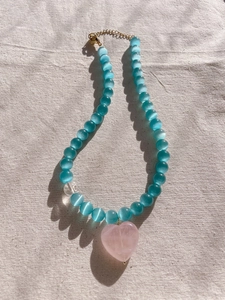 Detail of glacier blue cat eye beads with a pink heart pendant on beige linen fabric