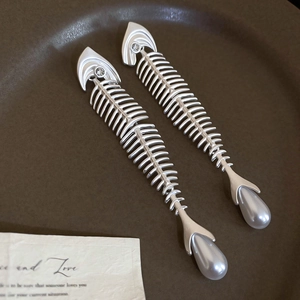 Macro detail of silver fishbone earrings with zircon head and water drop pearl charms