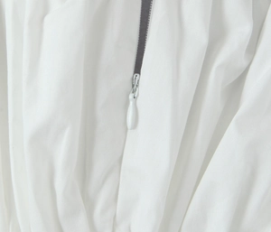 Détail de la fermeture éclair grise sur une robe blanche à manches bouffantes
