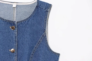 Gros plan détaillé du gilet en jean bleu avec boutons métalliques et coutures sur fond blanc