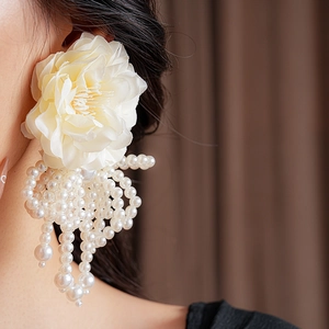 Detailed view of cream fabric flower earrings with elegant pearl tassels on a model