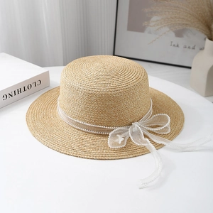 Detail of flat-top straw hat with elegant white mesh ribbon and pearl bow accents
