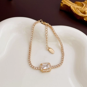 Detailed view of a gold tennis bracelet with a large rectangular zircon on a white plate