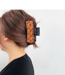 Rear view of woman wearing orange and black Halloween pumpkin claw clip with text