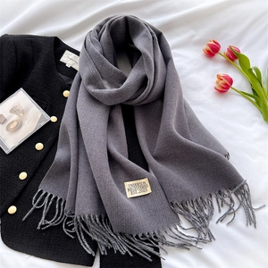 Detail of grey cashmere-feel scarf with fringe edges and beige minimalist tag