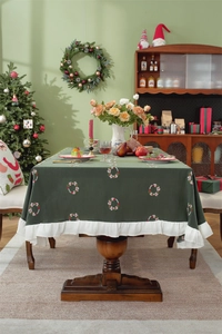 Close-up of dark green Christmas tablecloth featuring embroidered wreaths and white ruffled edges