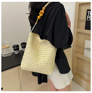 Detail of a straw woven tote bag featuring unique wooden bead shoulder straps on a model