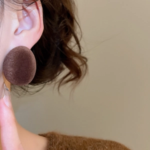 Détail de boucles d'oreilles ovales floquées marron foncé avec texture velours