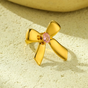 Elegant gold bow ring featuring a pink oval gemstone centerpiece on a textured background