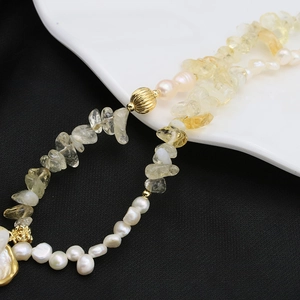 Baroque pearl and yellow crystal necklace with gold beads on black and white background