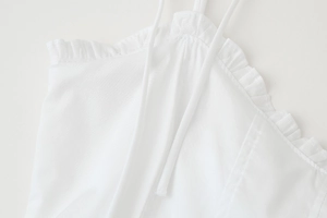 Detail of white spaghetti strap top featuring delicate ruffled edges and fine fabric texture