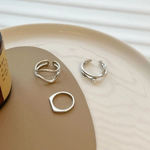 Three minimalist silver geometric rings set with pearl detail on a beige tray