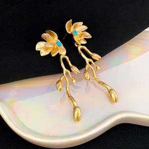 Detail of golden metal leaf earrings with turquoise inlay on a pearl white base