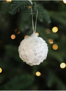 Sparkling white sequined Christmas ball ornament hanging on a pine tree with warm bokeh light