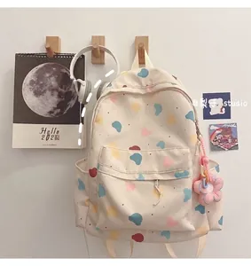 Detail of cream backpack with cartoon bear prints and pink flower plush keychain