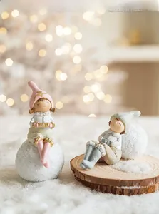 Close-up of resin Christmas angel girl figurines with pink and blue hats on snow base