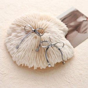 Minimalist silver bow earrings with snake chain texture on white coral decor