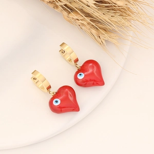 Gold heart drop earrings with red enamel and blue evil eye charm on minimalist background