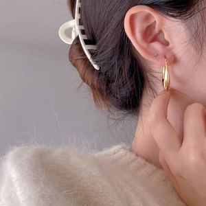 Close-up of minimalist gold U-shape teardrop earring worn with a cozy mohair sweater