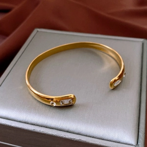 Detail of gold open bracelet with rectangular and round cubic zirconia on silk background