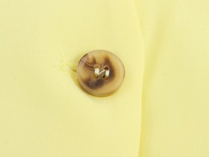 Dettaglio macro del tessuto twill giallo ad alta densità e del bottone marrone in tartaruga