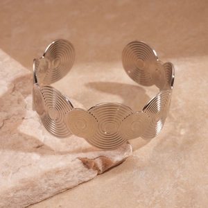 Detail of silver cuff bracelet with concentric geometric spiral patterns on stone background