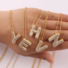 Close-up of golden bubble letter pendants with sparkling crystals held in hand