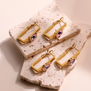 Golden rectangular hoop earrings with purple zircon stones on elegant stone display