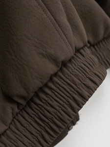 Detailed close-up of dark brown faux leather jacket with elastic hem and stitching