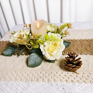Detail of a lit LED candle inside a cream rose wreath with green leaves on a lace runner
