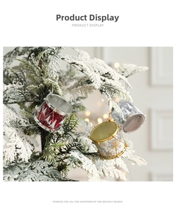 Detail of red and gold Christmas drum ornaments hanging on snowy pine branches with lights