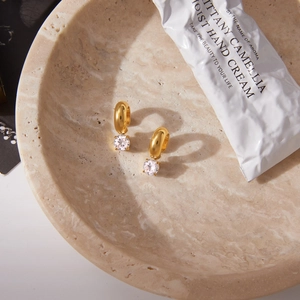 Elegant gold titanium earrings with round zircon stones on a beige textured stone tray