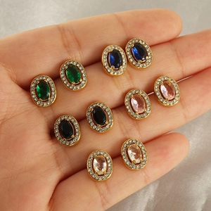 Five pairs of oval zircon stud earrings in gold finish displayed on grey silk fabric