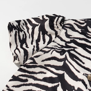 Makro-Detail des Zebra-Satin-Stoffs mit dekorativem goldenem Knopf am Ärmelaufschlag