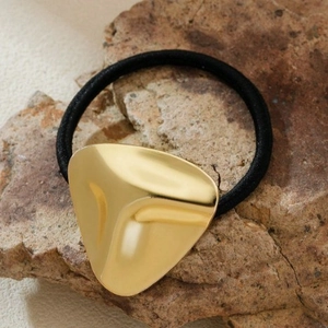 Elastic hair tie with a textured gold geometric metal piece on a natural stone surface