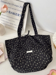 Floral black pleated tote bag with yellow flowers and tie closure on white desk
