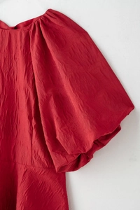 Gros plan sur un tissu rouge foncé texturé avec détail de manche bouffante et plis élégants