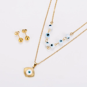 Close-up of golden necklace and stud earrings set with blue evil eye charms