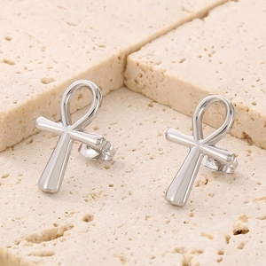 Macro shot of polished silver Ankh cross stud earrings on a natural stone base