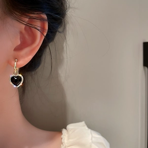 Detail of a gold heart hoop earring with black gemstone and rhinestones on a model